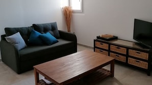 A living room with a dark green sofa, a wooden coffee table, a TV on a stand, and a window providing natural light. - Joli T1 au Calme, Entre Collines et Littoral; Idéal Pour Explorer la Région! (Gémenos)