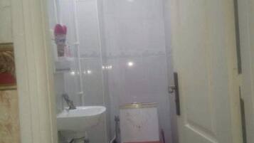 A narrow bathroom with a white sink, a toilet with a red seat, and a shower area.
