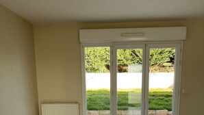 A room with a large sliding glass door leading to an outdoor area with a tiled patio and a grassy lawn. - Chambre Chez Lhabitant (Cholet)