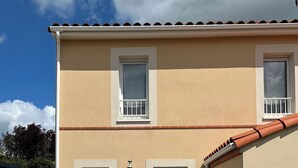 A two-story building with a beige exterior, a tiled roof, and a paved driveway. - Chambre Chez Lhabitant (Cholet)