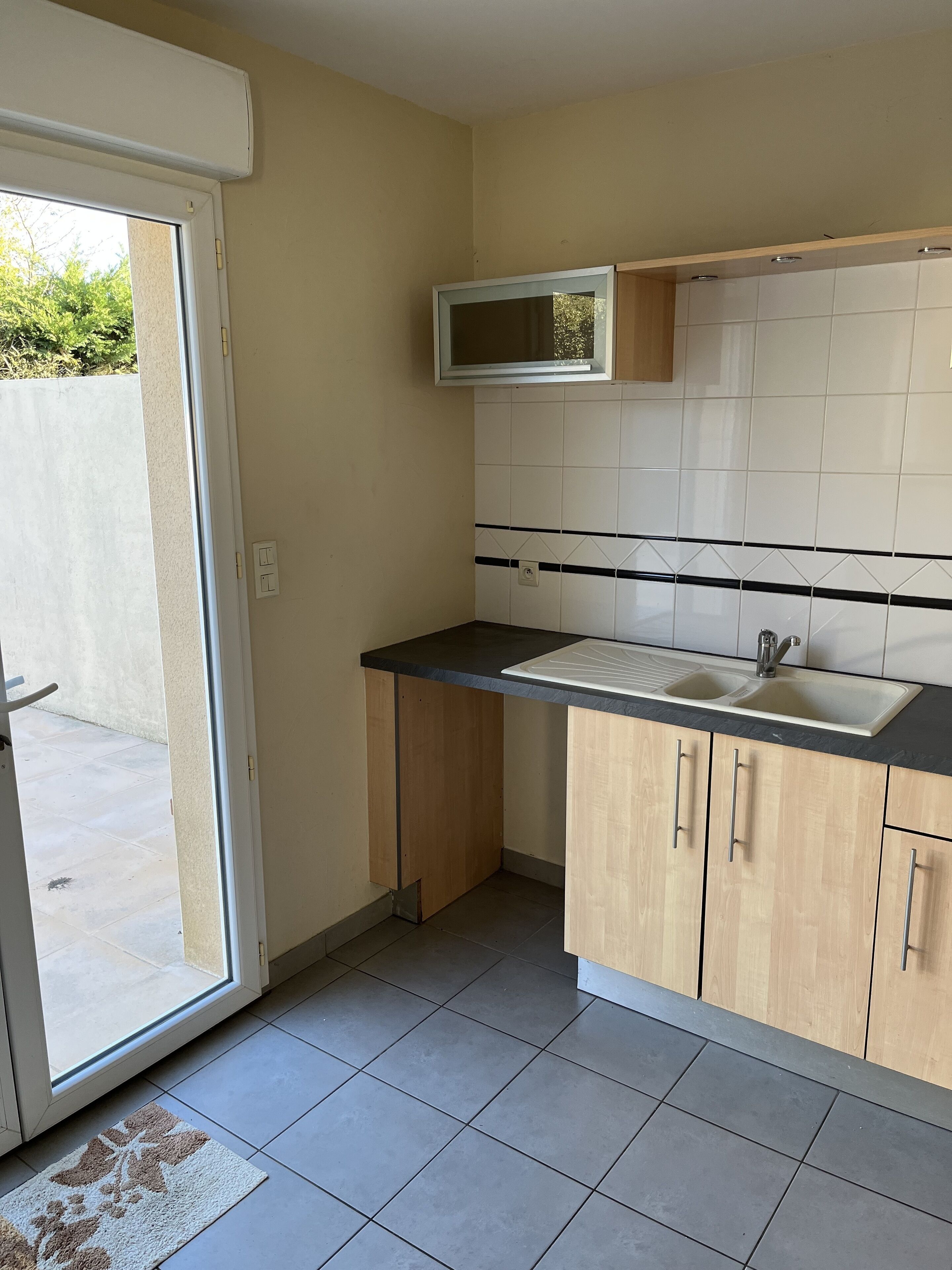 A small kitchen with a sink, wooden cabinets, a microwave, and a tiled backsplash.