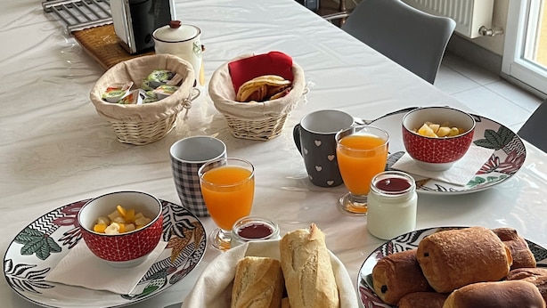 A breakfast table with bread, fruit, and juice. - Chambre Chez Lhabitant (Cholet)