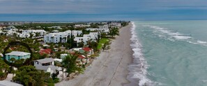 A coastal residential area with beachfront properties, including houses with red roofs and white exteriors, surrounded by greenery and a sandy beach.