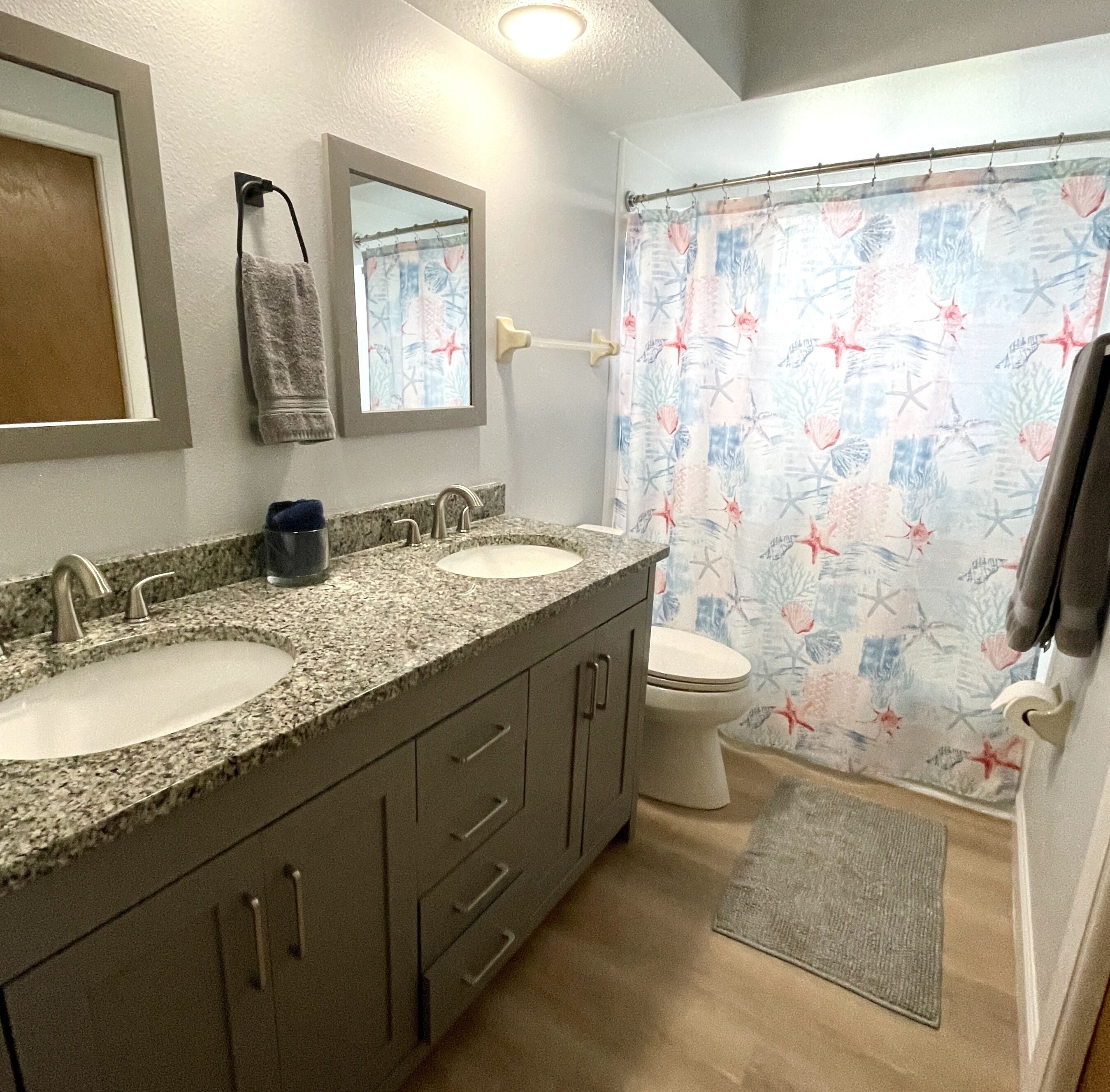 Un baño con dos lavamanos, un inodoro y una cortina de ducha con motivos marinos.