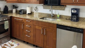 A modern kitchen with wooden cabinets, granite countertops, a stainless steel sink, a coffee maker, and a dishwasher. - Charming Townhouse 12 minutes to Boston (Watertown)
