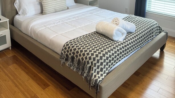 A neatly made bed with a patterned throw blanket, a bedside lamp, and framed artwork on the wall. - Charming Townhouse 12 minutes to Boston (Watertown)
