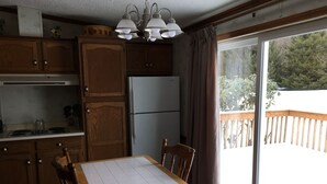 Une cuisine avec des meubles en bois, un réfrigérateur, une table à manger avec des chaises et une porte-fenêtre coulissante donnant sur une terrasse.