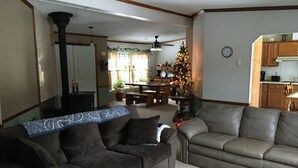 Un salon avec deux canapés, une table basse, une cheminée, un coin repas agrémenté d’un sapin de Noël, et une cuisine visible à travers une porte ouverte.