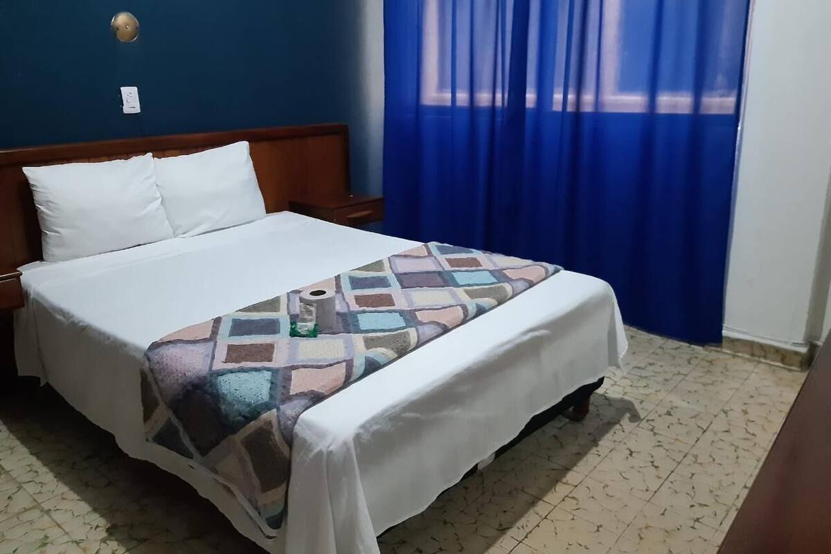 Una cama bien hecha con un edredón estampado, un cabecero de madera y una cortina azul.