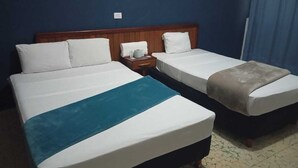Habitación de hotel con dos camas, cabecera de madera, mesita de noche y cortina azul.