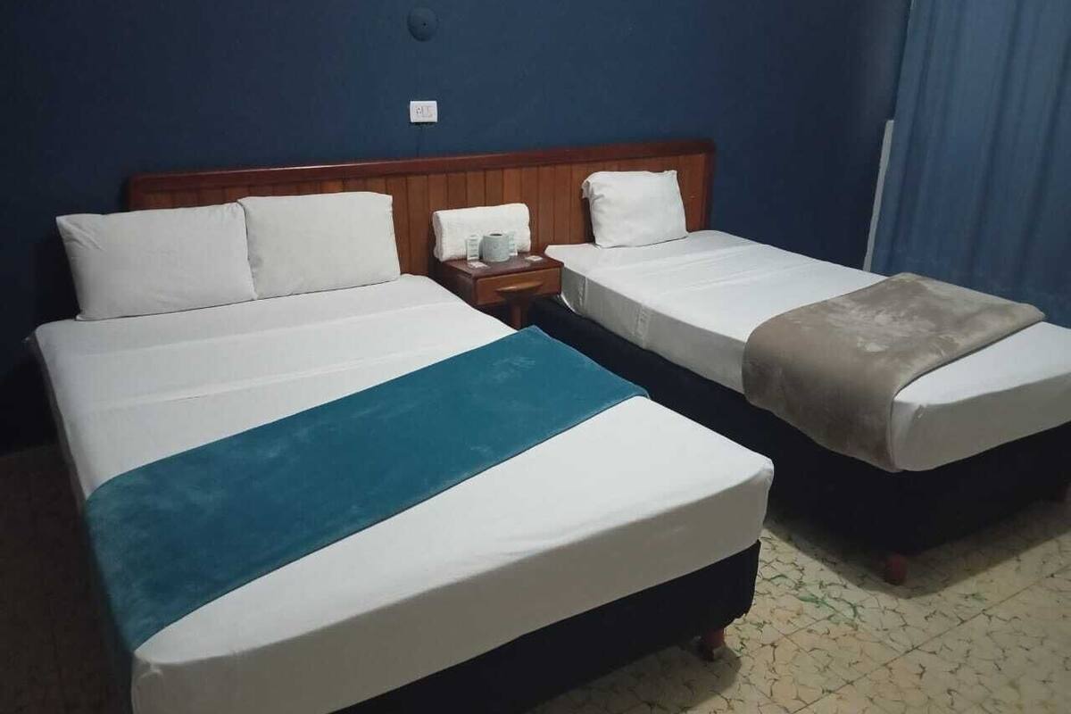 Habitación de hotel con dos camas, cabecera de madera, mesita de noche y cortina azul.