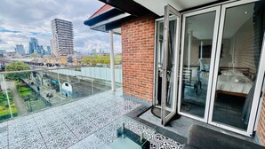 A balcony with patterned floor tiles, a glass door leading to a bedroom, and a cityscape view. - London Bridge: Private Rooftop Terrace 3BR-7Guests (London)