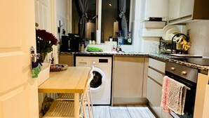 A compact kitchen with a washing machine, a dining table, and a small window with curtains. - London Bridge: Private Rooftop Terrace 3BR-7Guests (London)