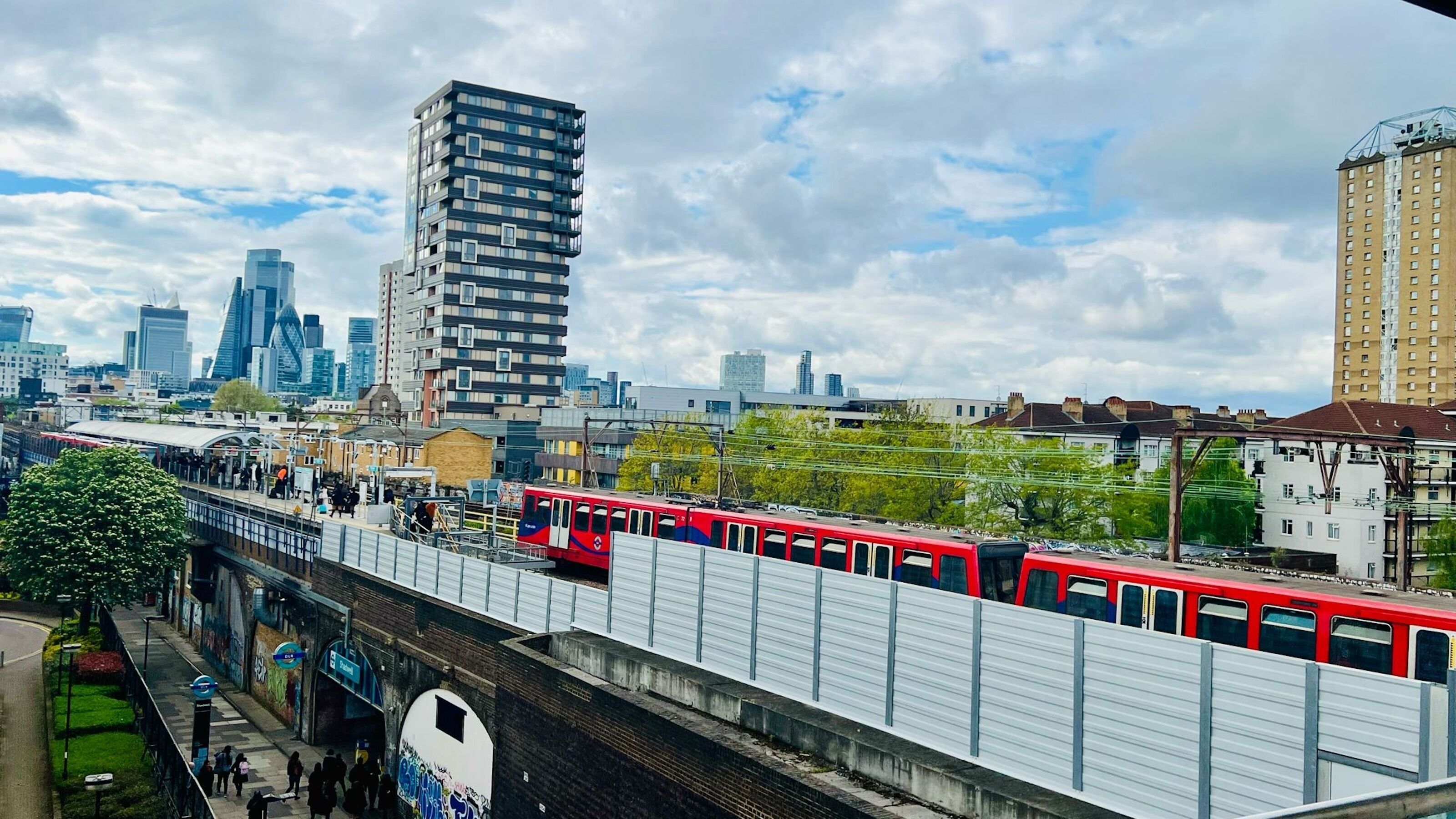 Un train rouge circule sur une voie surélevée, avec une vue sur la ville en arrière-plan.