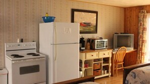 A compact kitchen with a stove, refrigerator, microwave, and a television. - CLIPPER SHIPP BEACH MOTEL (Pocologan)