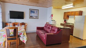 A living room with a red leather sofa, a dining table with floral tablecloth, a TV, and a framed picture on the wall. - CLIPPER SHIPP BEACH MOTEL (Pocologan)