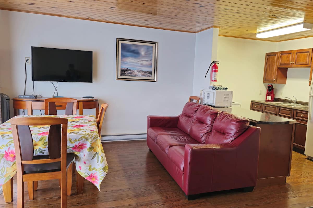 Un salón con un sofá de cuero rojo, una mesa de comedor con mantel floral, un televisor y un cuadro en la pared.