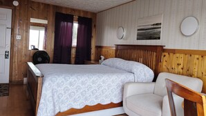 A bedroom with a bed, a chair, a bedside table, a mirror, and a window with curtains. - CLIPPER SHIPP BEACH MOTEL (Pocologan)