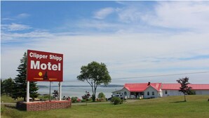 A motel sign with a moose and a sunset, a red-roofed building, and a grassy area with trees. - CLIPPER SHIPP BEACH MOTEL (Pocologan)