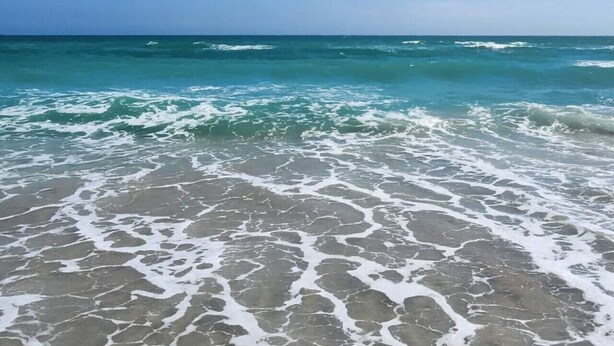 Une plage à l’eau d’un bleu limpide et aux vagues d’écume blanche.