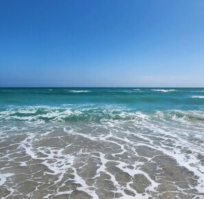Ein Strand mit klarem, blauem Wasser und weißen Schaumwellen.