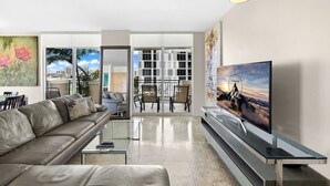 Un salon moderne avec un canapé en cuir, une table basse en verre, un téléviseur à écran plat et un balcon offrant une vue sur la ville.