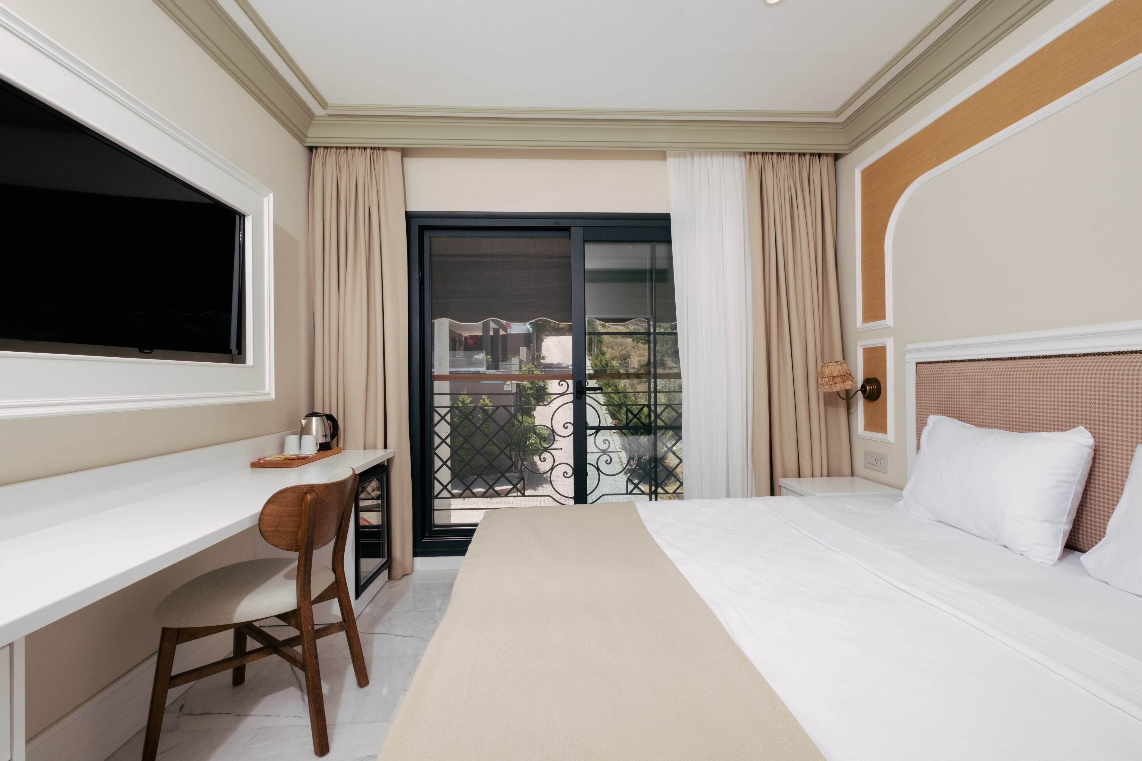 A hotel room with a bed, a desk, a chair, a TV, and a balcony with curtains.