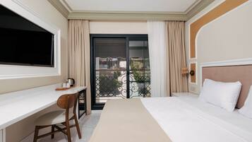 A hotel room with a bed, a desk, a chair, a TV, and a balcony with curtains.