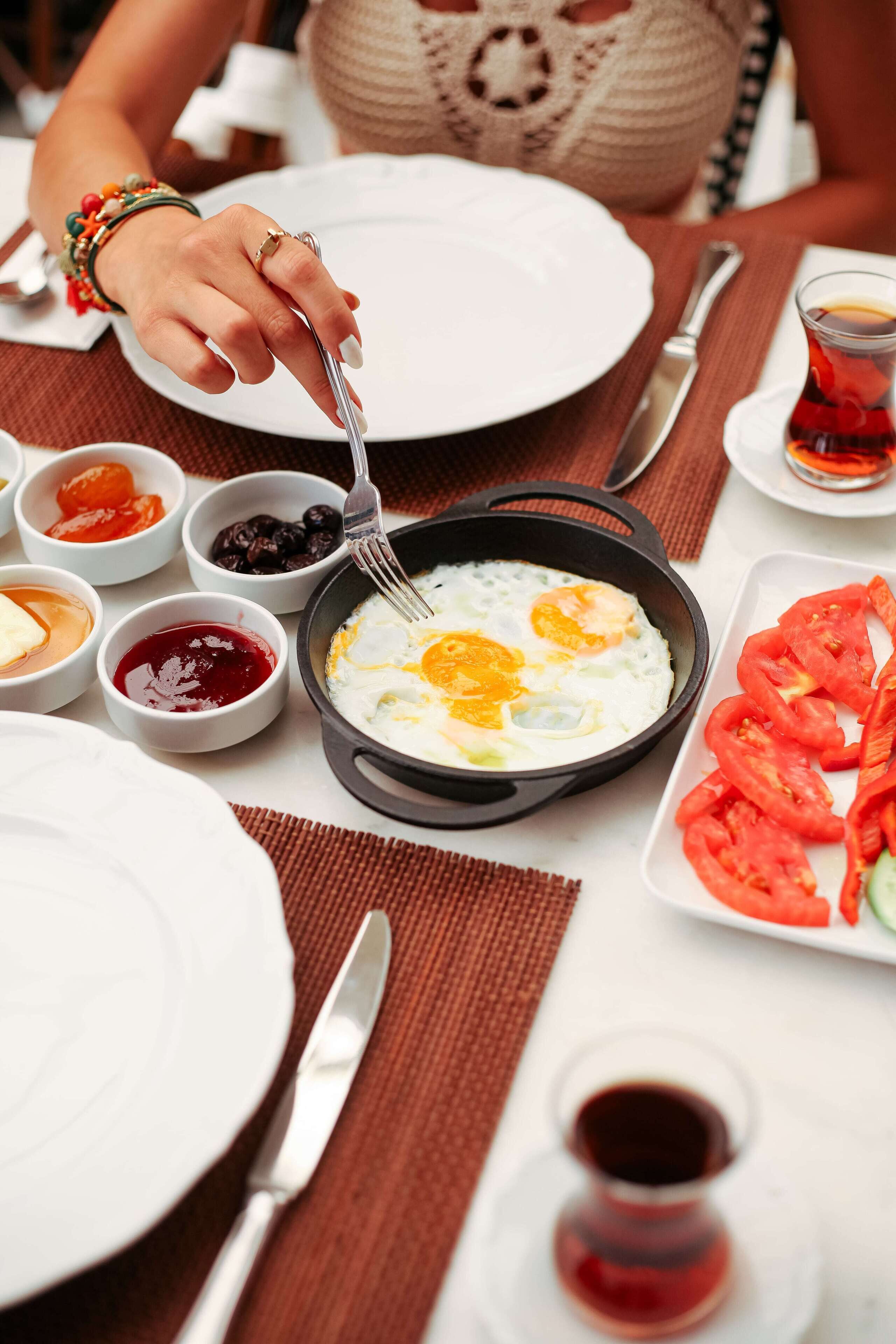 Un desayuno con un plato de huevos, diferentes condimentos y una taza de té.