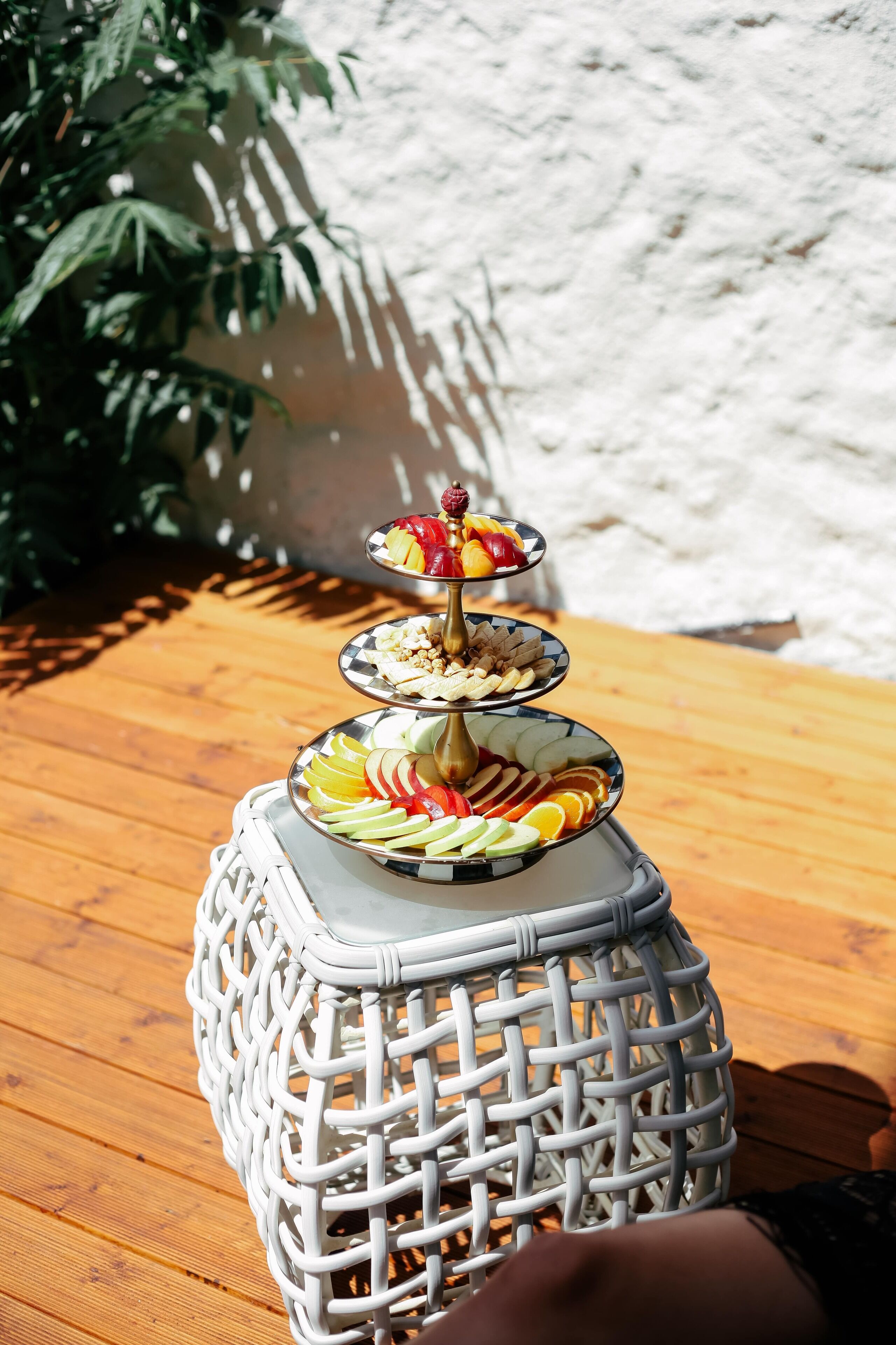 A tiered fruit and nut display on a wicker table outdoors.