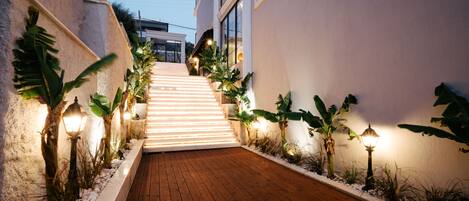 A wooden pathway leading to a building with white walls and a staircase.