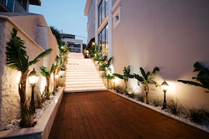 A wooden pathway leading to a building with white walls and a staircase.