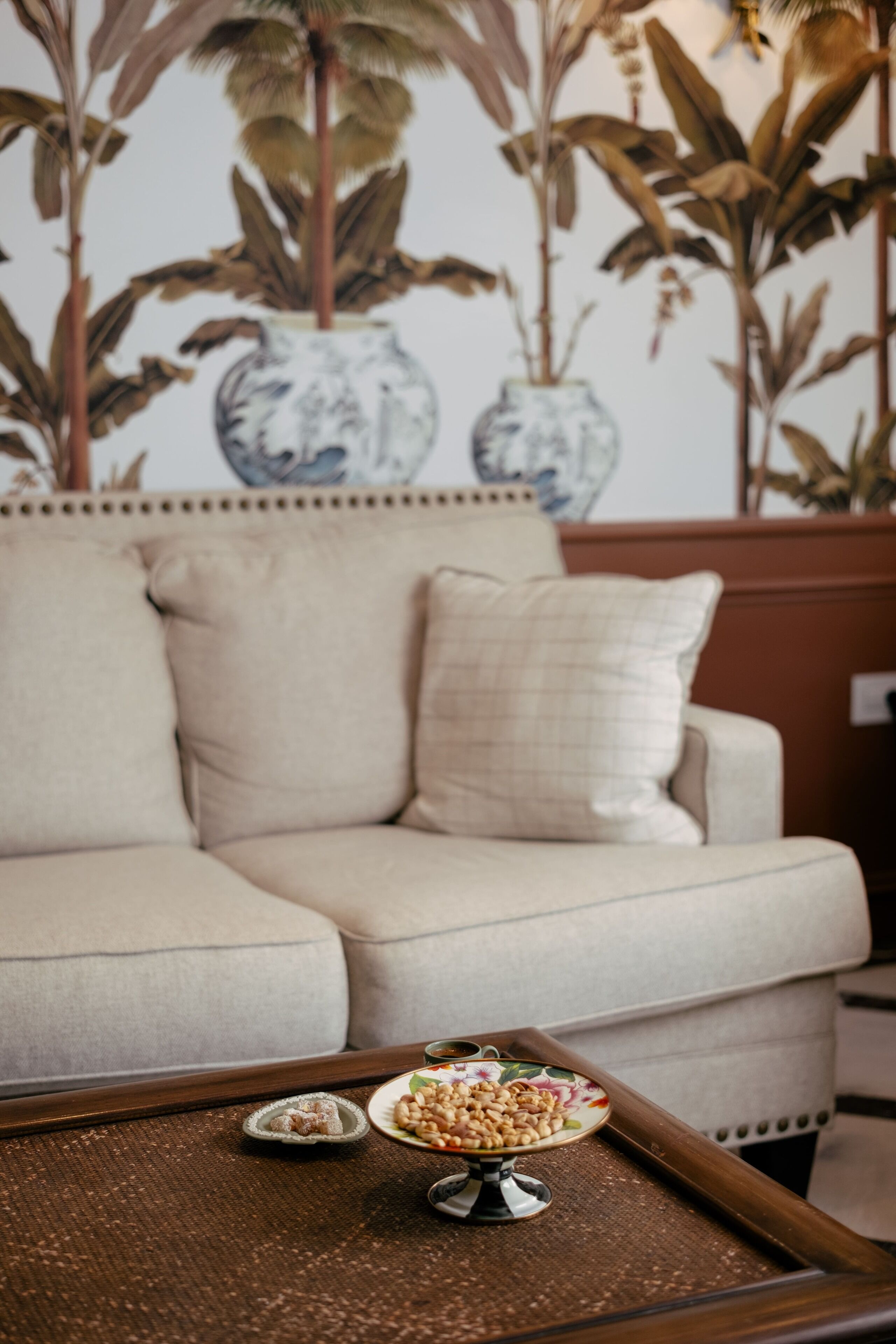 A beige sofa with a decorative pillow, a tray with snacks, and a wall with large plant prints.