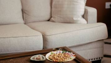 A beige sofa with a decorative pillow, a tray with snacks, and a wall with large plant prints.