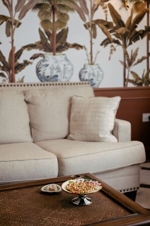 A beige sofa with a decorative pillow, a tray with snacks, and a wall with large plant prints. - DBD Hotel Çeşme (Cesme)
