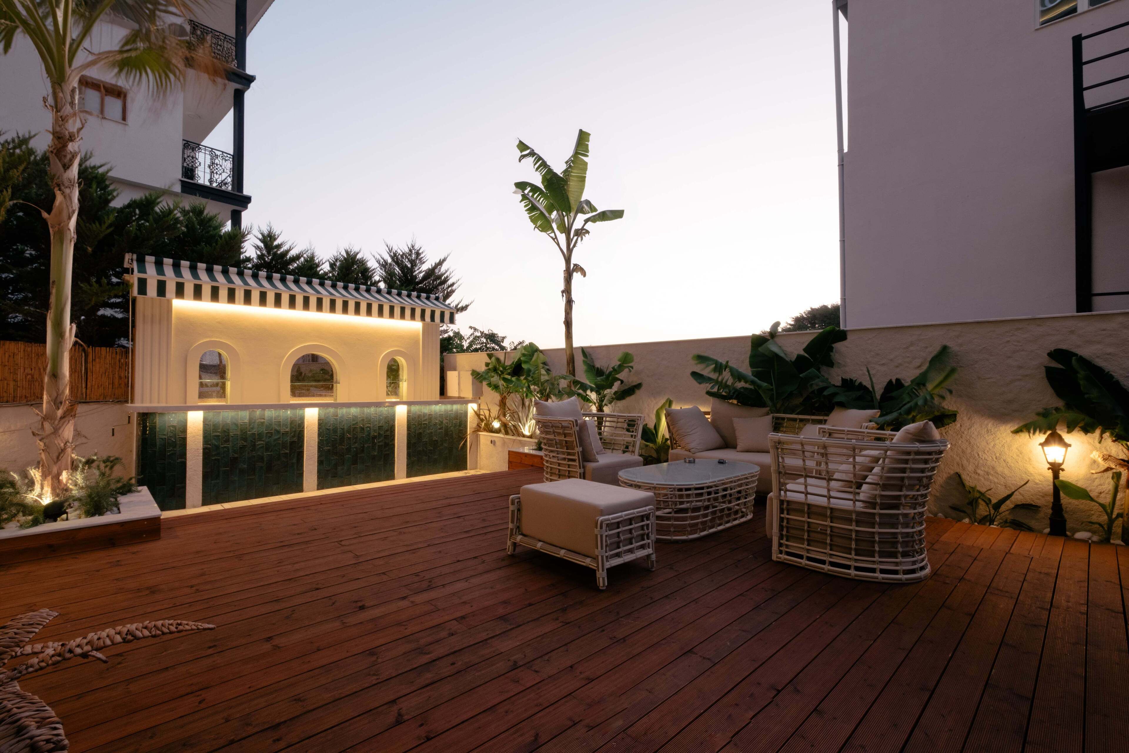 Terraza de madera con mobiliario exterior, una pequeña barra y plantas en macetas.
