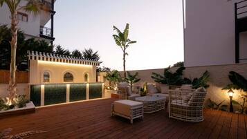Terraza de madera con mobiliario exterior, una pequeña barra y plantas en macetas.