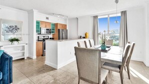 A modern kitchen with white cabinetry, a central island, and a dining area with a table and chairs. - LUXURY KINGDAVID*3/2H*KINGBEDROOM*BEST LOCATION (Sunny Isles Beach)