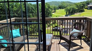 A deck with wicker furniture and a view of a green landscape.