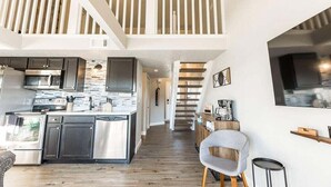 A modern kitchen with stainless steel appliances, a wooden floor, and a staircase leading to a loft area.