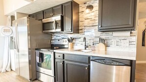 A modern kitchen with stainless steel appliances, dark cabinetry, and a stone backsplash.