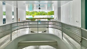 A modern interior with a curved glass railing, a ceiling fan, and a view of greenery outside.