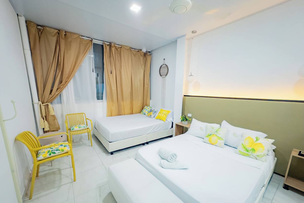A hotel room with a bed, a chair, a small table, and a window with curtains.