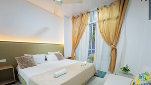 A hotel room with a bed, a nightstand, a window with curtains, and a small table with a plant.