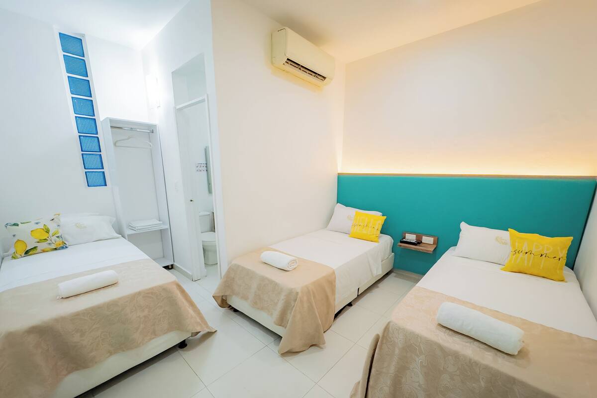 A hotel room with three beds, a bathroom, and an air conditioning unit.