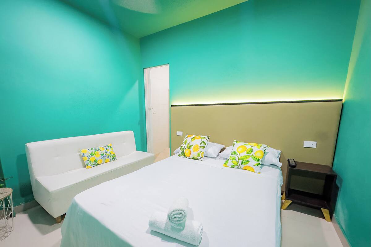 A hotel room with a bed, a white sofa, and a nightstand.