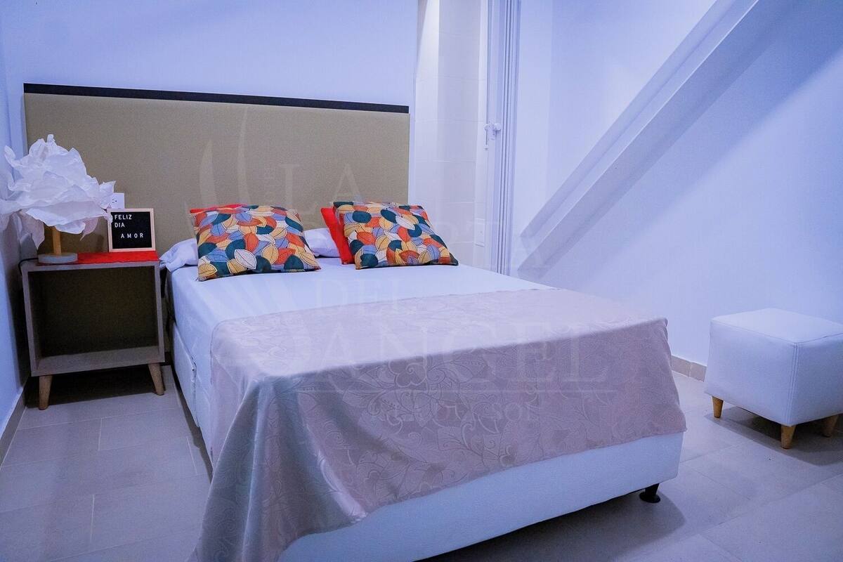 A neatly arranged bedroom with a bed, pillows, a bedside table, and a small stool.