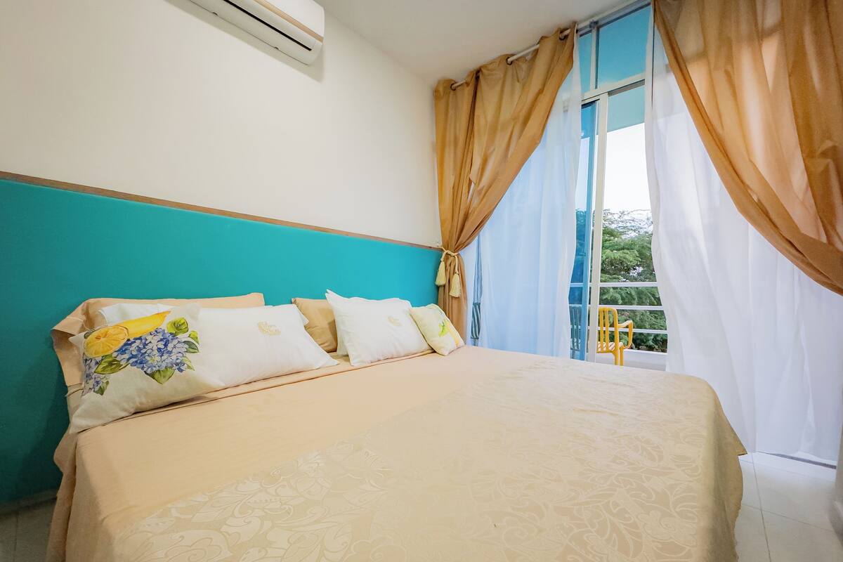 A bed with a floral bedspread, a window with curtains, and a view of greenery outside.