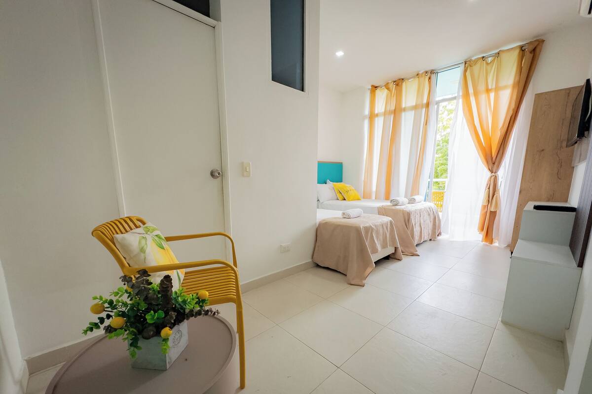 A hotel room with two beds, a chair, a small table with a plant, and a view of the outdoors.