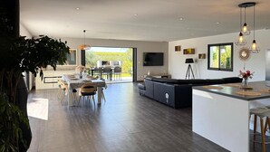 A modern kitchen with a dining area, large windows, and a view of the outdoors.